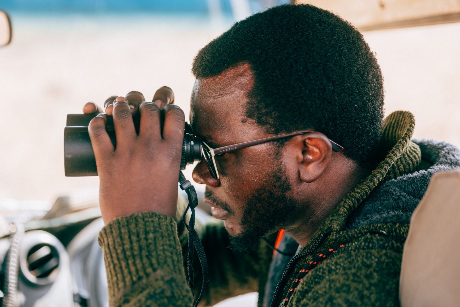 Sylvester scanning the plains with binoculars from the Land Cruiser